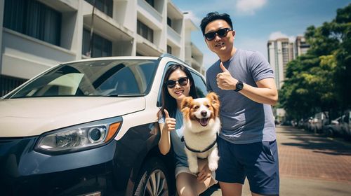 A man and his girlfriend smiling, and giving the thumbs up, while carrying their dog.